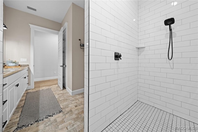 full bathroom with baseboards, visible vents, a tile shower, and vanity