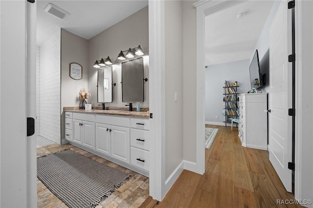 bathroom featuring a sink, wood finished floors, visible vents, baseboards, and double vanity