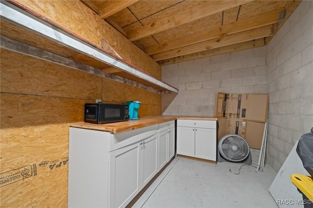 kitchen featuring concrete block wall, black microwave, concrete floors, white cabinetry, and wooden counters