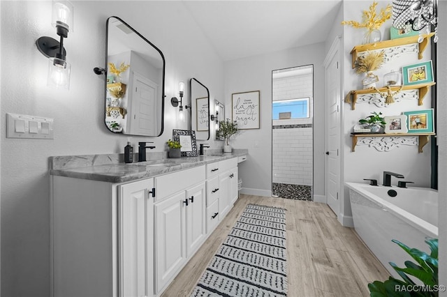 bathroom with double vanity, wood finished floors, walk in shower, a freestanding bath, and a sink