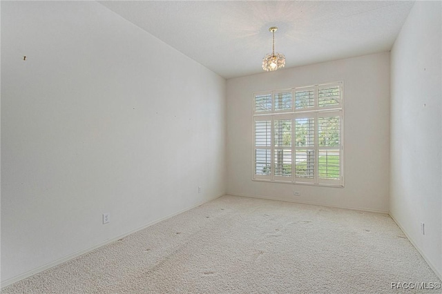 carpeted empty room featuring an inviting chandelier