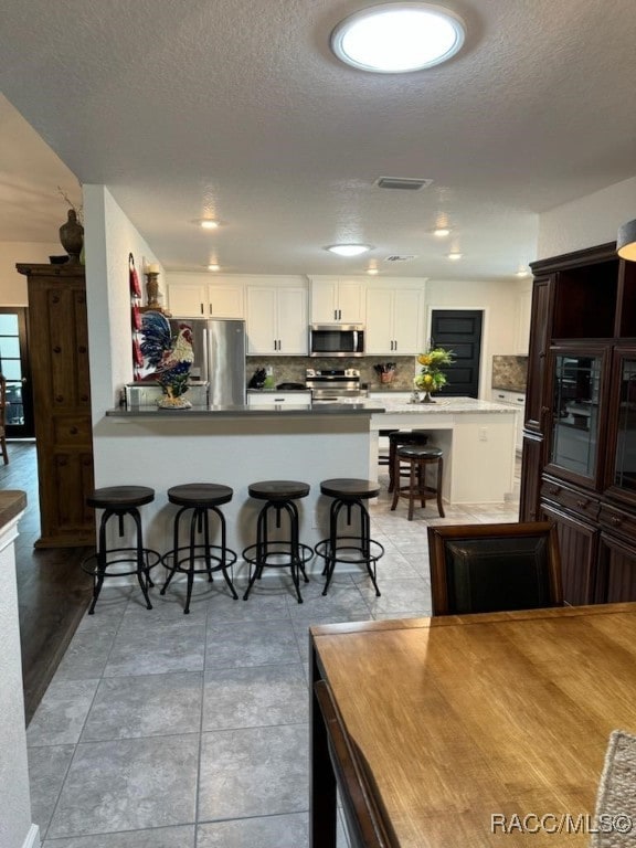 kitchen featuring a textured ceiling, white cabinetry, a breakfast bar area, and appliances with stainless steel finishes