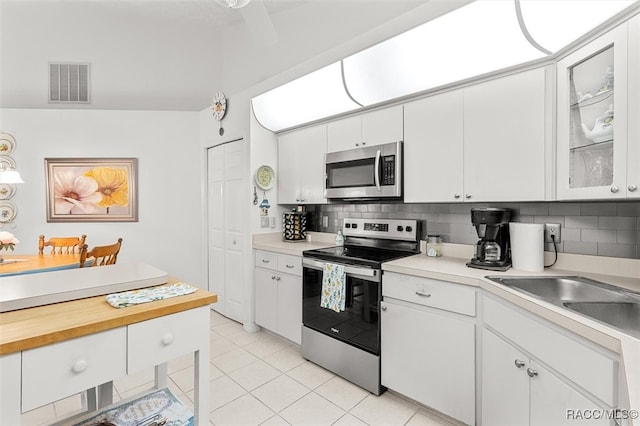 kitchen featuring backsplash, stainless steel appliances, sink, light tile patterned floors, and white cabinetry