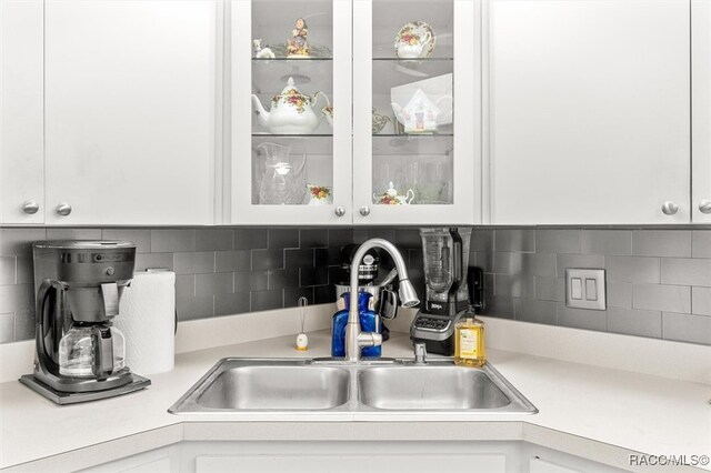 kitchen with backsplash, white cabinetry, and sink