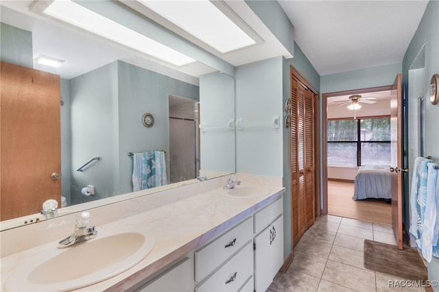 ensuite bathroom featuring tile patterned flooring, double vanity, a skylight, and a sink