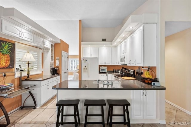 kitchen featuring a kitchen bar, white cabinets, white appliances, and kitchen peninsula