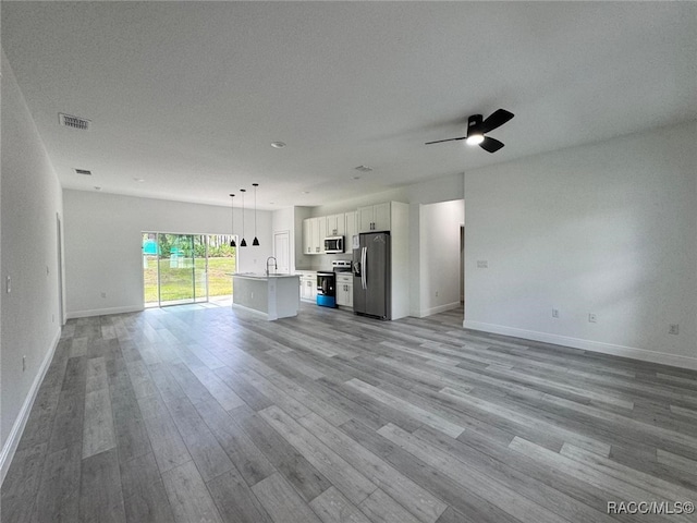 7549 N Santos Dr, Citrus Springs, FL 34434 - unfurnished living room with baseboards, light wood-style flooring, a sink, ceiling fan, and a textured ceiling