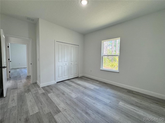 7549 N Santos Dr, Citrus Springs, FL 34434 - unfurnished bedroom featuring baseboards, light wood-style flooring, a textured ceiling, and a closet