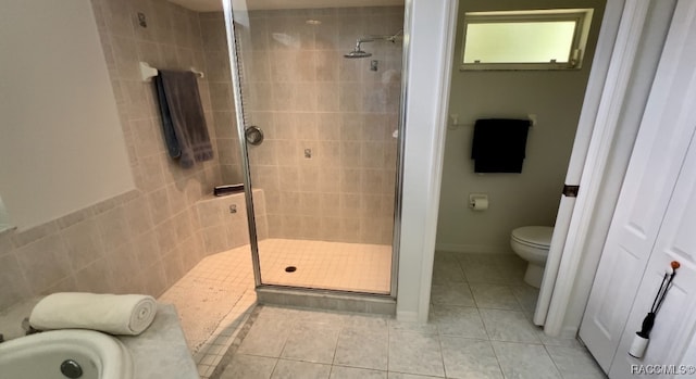 bathroom with tile patterned floors, toilet, tiled shower, and tile walls