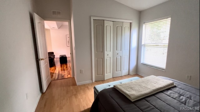 bedroom with light hardwood / wood-style floors, vaulted ceiling, and a closet