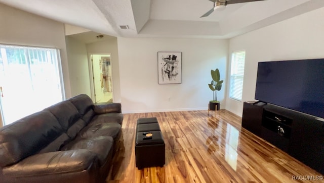 living room featuring hardwood / wood-style floors, ceiling fan, and a raised ceiling