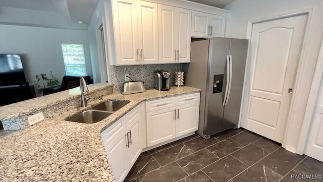 kitchen featuring backsplash, sink, stainless steel fridge, light stone countertops, and white cabinetry