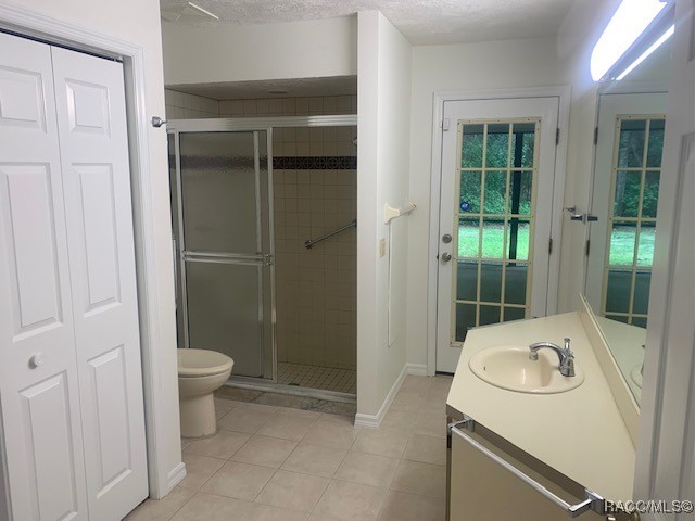 bathroom with tile patterned flooring, vanity, a shower with shower door, and toilet