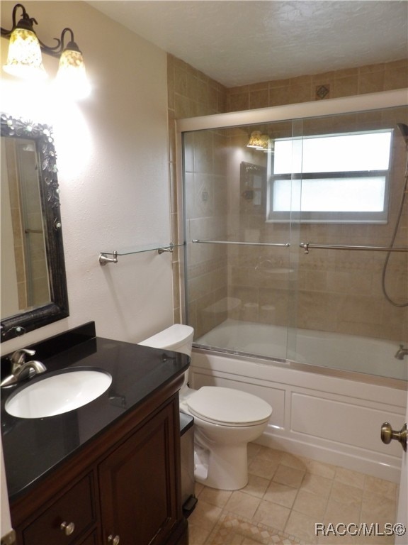 full bathroom featuring combined bath / shower with glass door, a textured ceiling, vanity, tile patterned flooring, and toilet