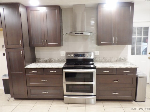 kitchen with double oven range, backsplash, wall chimney exhaust hood, dark brown cabinets, and light stone counters