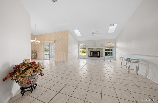 tiled living room featuring a fireplace, ceiling fan with notable chandelier, a skylight, and high vaulted ceiling