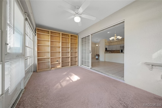 carpeted empty room featuring ceiling fan with notable chandelier