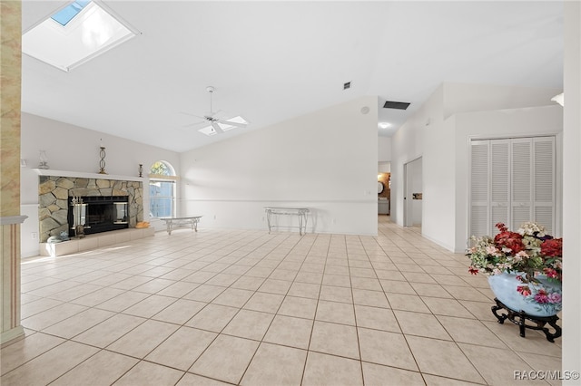 unfurnished living room with a stone fireplace, ceiling fan, vaulted ceiling with skylight, and light tile patterned floors