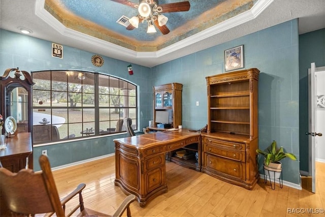 office space with a tray ceiling, light wood-style flooring, visible vents, and ornamental molding