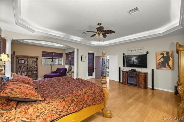 bedroom with visible vents, light wood-style flooring, arched walkways, a raised ceiling, and ornate columns