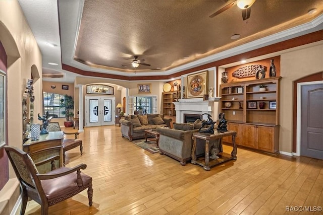 living area with light wood-style flooring, a fireplace, arched walkways, french doors, and a raised ceiling