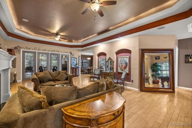 living area featuring a raised ceiling, light wood-style flooring, a fireplace, and a healthy amount of sunlight