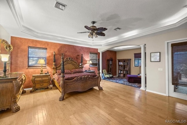 bedroom with visible vents, a tray ceiling, hardwood / wood-style floors, arched walkways, and ornate columns