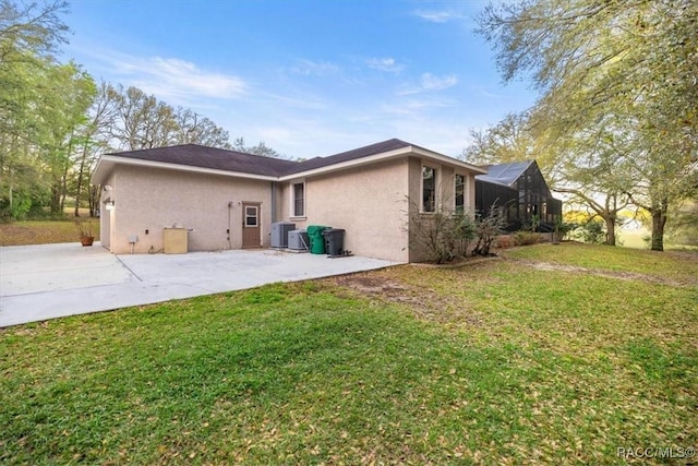 view of side of home with glass enclosure, a patio, a yard, central AC, and stucco siding