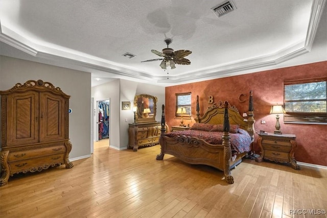 bedroom with a walk in closet, a raised ceiling, visible vents, and light wood-style flooring