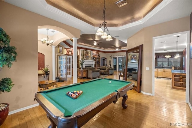 game room featuring visible vents, light wood-type flooring, decorative columns, arched walkways, and a raised ceiling