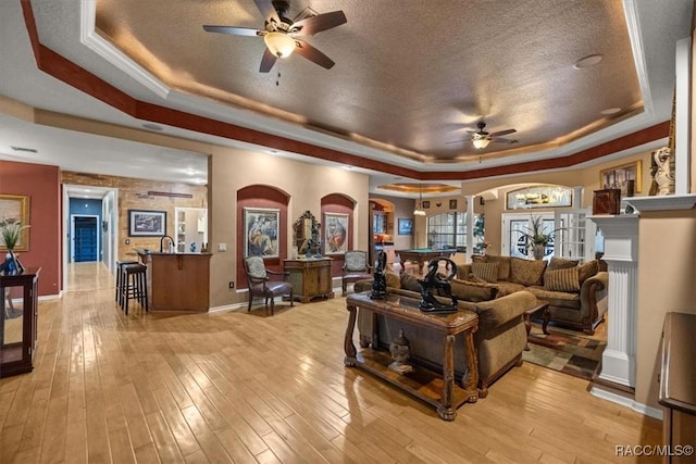 living area featuring arched walkways, a textured ceiling, a raised ceiling, and light wood-style floors