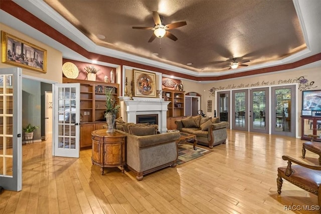 living area with french doors, light wood-style floors, and a tray ceiling