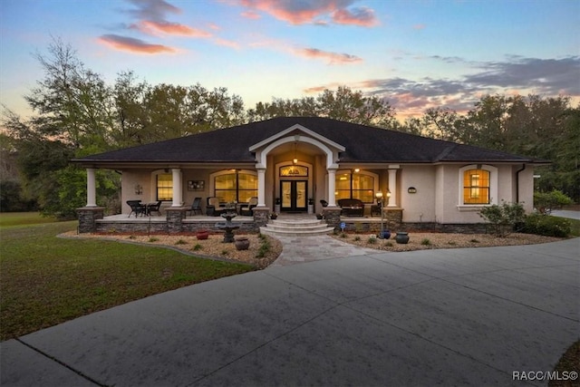 view of front of house with stucco siding, a porch, french doors, and a front yard