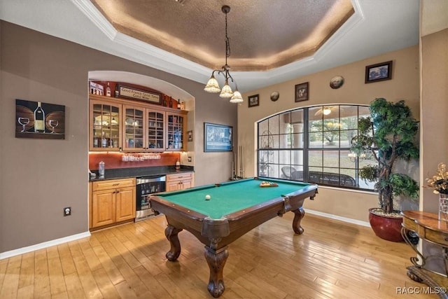 recreation room with wine cooler, a raised ceiling, wet bar, and light wood-style flooring