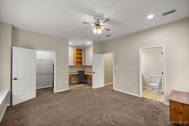 unfurnished bedroom with baseboards, visible vents, a walk in closet, dark carpet, and connected bathroom