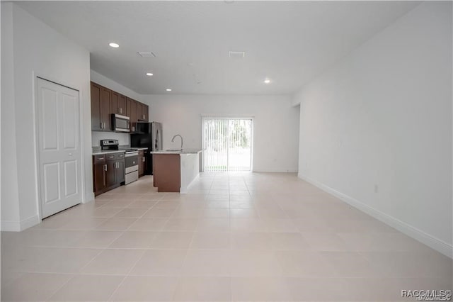 kitchen featuring light tile patterned floors, dark brown cabinetry, stainless steel appliances, and a kitchen island with sink