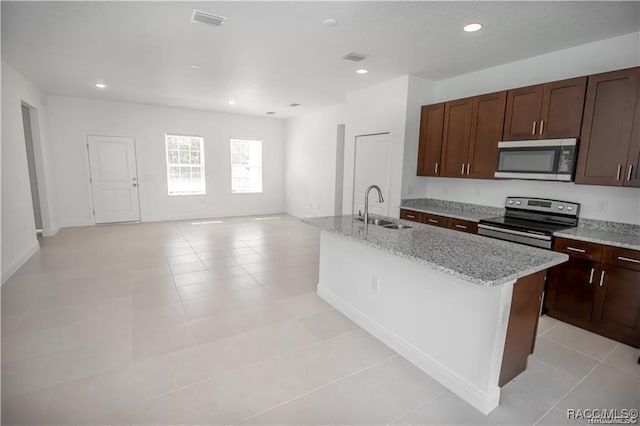 kitchen featuring appliances with stainless steel finishes, light stone counters, a kitchen island with sink, sink, and light tile patterned floors