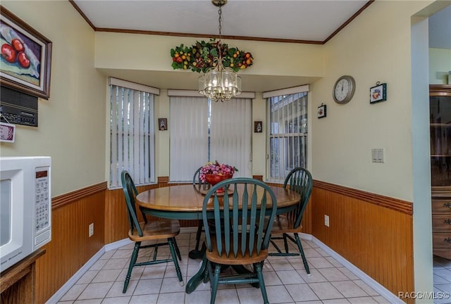 dining area with light tile patterned floors, wainscoting, crown molding, wood walls, and a notable chandelier