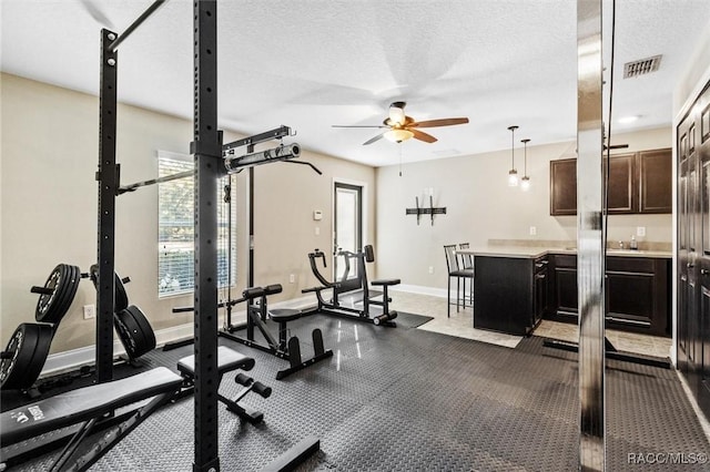 gym featuring ceiling fan, sink, and a textured ceiling