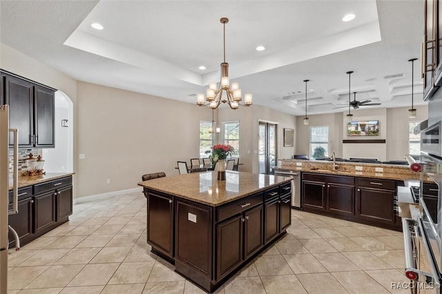 kitchen with pendant lighting, a tray ceiling, a center island, and light stone counters