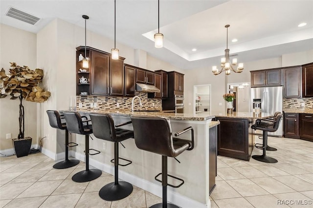 kitchen with decorative light fixtures, dark brown cabinets, light stone countertops, and a breakfast bar