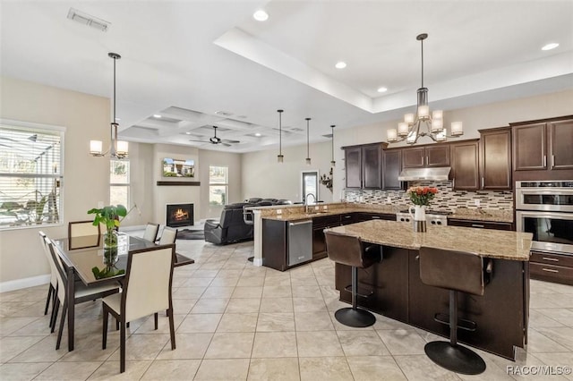 kitchen featuring hanging light fixtures, light stone countertops, appliances with stainless steel finishes, and a kitchen bar