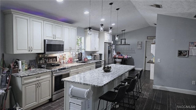 kitchen featuring a breakfast bar area, stainless steel appliances, a kitchen island, white cabinets, and decorative light fixtures