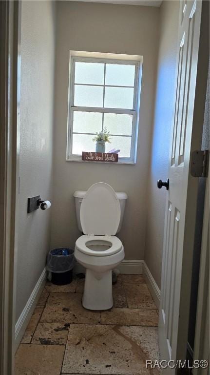 bathroom featuring stone tile floors, toilet, and baseboards