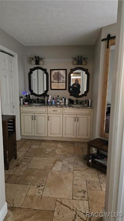 full bathroom featuring a textured ceiling, double vanity, a sink, and stone tile floors