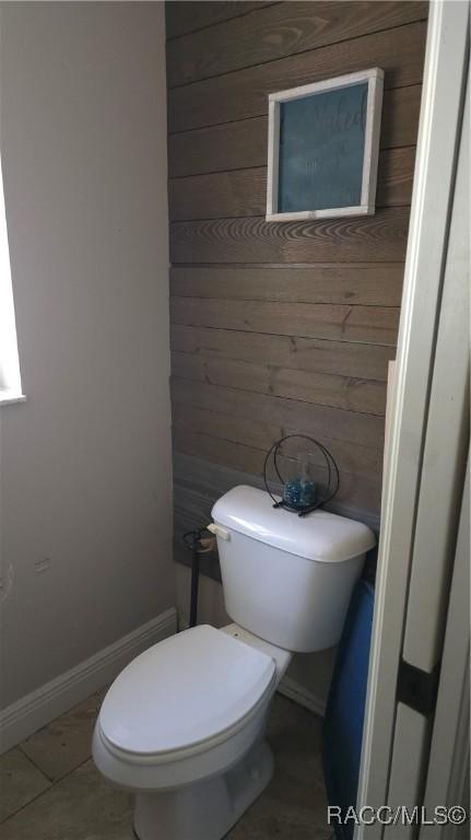 bathroom with baseboards, tile patterned floors, toilet, and wooden walls