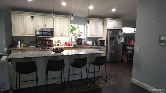 kitchen with stone countertops, a kitchen breakfast bar, appliances with stainless steel finishes, a center island, and pendant lighting