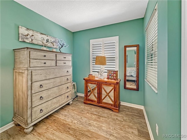 interior space featuring light wood-style flooring, baseboards, and a textured ceiling