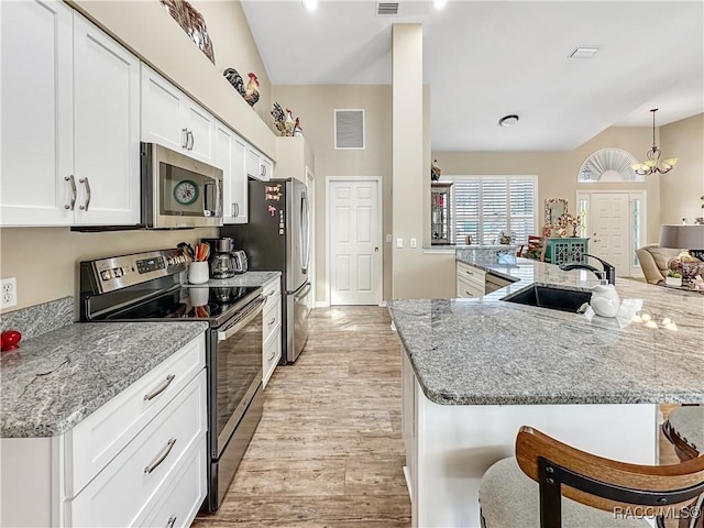 kitchen featuring visible vents, a breakfast bar area, stainless steel appliances, light wood-type flooring, and a sink