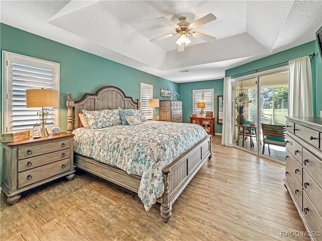 bedroom featuring access to exterior, a tray ceiling, a textured ceiling, and light wood finished floors